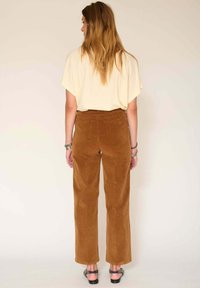 Un pantalon large en velours côtelé marron avec des poches arrière, associé à un haut beige à col montant. Les pantalons ont une coupe droite et un tissu texturé.