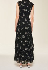 Svart blommig maxiklänning med volangärmar, lagerdesign och gröna och vita blommönster; har en figursydd midja och semi-transparent tyg.