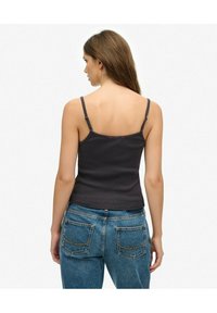Donkergrijs geribd tanktop met dunne banden, heeft een strak design en een naadloze achterkant. Gepaard met hooggetailleerde blauwe jeans.