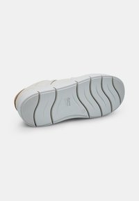 Semelle de sneaker blanche avec une surface en caoutchouc texturée, présentant un motif de bande de roulement ondulé et un petit logo en relief. Éléments de design minimalistes.