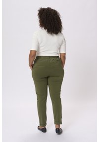 Pantaloni stretch verdi con una texture liscia e orli arrotolati; abbinati a una maglietta bianca aderente, visti da dietro.