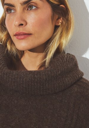Brauner, gestrickter Pullover mit einem breiten, gerippten Kragen. Weiche Textur, körpernahe Passform, betont die Gesichtszüge und den Hautton.