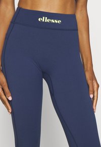 Marinblå leggings gjorda av stretchigt material med hög midja, med logotypen "ellesse" i gult på framsidan.