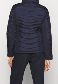 Giacca puffer blu navy con motivo trapuntato a chevron, materiale leggero, chiusura con zip frontale e colletto alto, dotata di maniche lunghe e polsini elasticizzati.