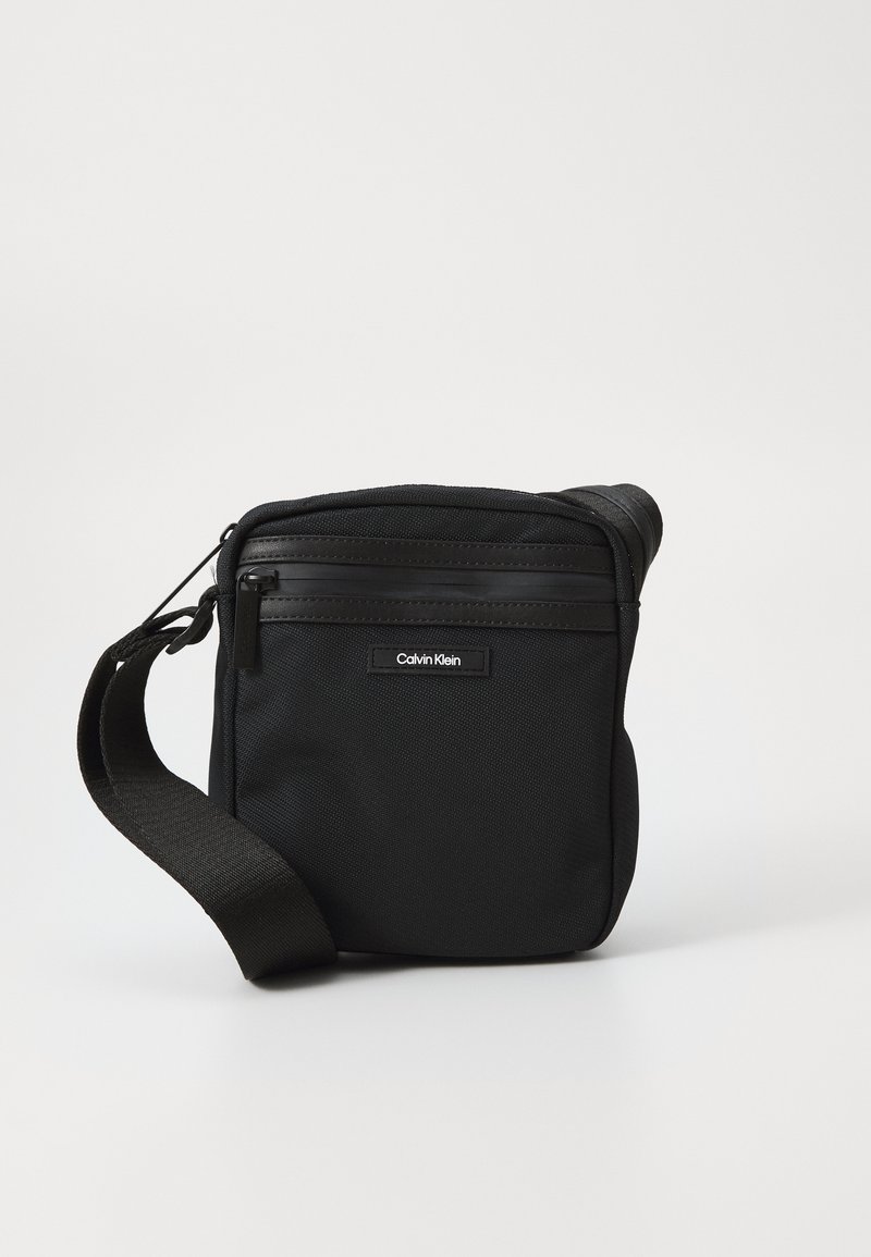 Borsa a tracolla nera realizzata in tessuto voluminoso con tracolla regolabile, dotata di chiusura superiore a zip e tasca con zip frontale. Logo Calvin Klein in evidenza.