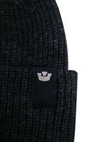 Bonnet en tricot noir avec une texture épaisse. Présente une étiquette de marque noire rectangulaire avec un logo gris à l'avant.