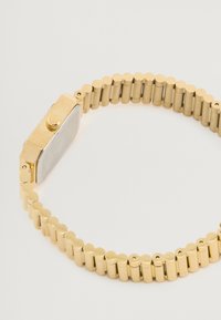 Guldtonet ur med et rektangulært urkasse og et fleksibelt armbånd med buede led. Uret har et simpelt design med en krone på siden.