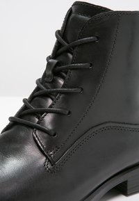 Stivale alla caviglia in pelle nera con finitura liscia, punta rotonda e design con lacci. Notevole cucitura a contrasto lungo i bordi.