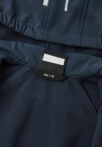 Jūrų pajėgų fliso striukės vidus su lygiu, tamsiai mėlynu pamušalu ir juodu etiketu, nurodančiu dydį 92. Yra elastingi rankogaliai ir siuvimo detalės.