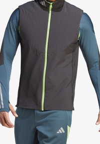 Chaqueta deportiva con cremallera con paneles en negro y azul, que presenta una sección superior texturizada, cremallera verde y detalles reflectantes en las mangas.