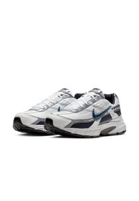 Sportieve sneakers met een witte mesh bovenkant, marineblauwe accenten en een zwarte rubberen zool; voorzien van een blauwe swoosh en getextureerde panelen.