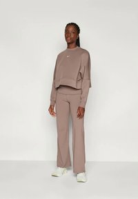 Brauner, verkürzter Sweatshirt mit Logo und passenden, hoch-taillierten Schlaghosen aus weichem Stoff, kombiniert mit weißen Sportsneakern.