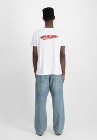 Hvid bomulds t-shirt med "industry" trykt i rød og sort på ryggen; parret med lyseblå, løstsiddende denim jeans.
