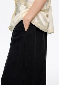 Lekka satynowa bluzka w kolorze kości słoniowej z koronkową lamówką, zestawiona z ciemną czarną spódnicą dżinsową z przednią kieszenią i pionowym przeszyciem.