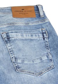 Jeans in denim azzurro chiaro con un'etichetta in pelle marrone sulla vita posteriore, caratterizzati da una singola tasca posteriore con dettagli cuciti.