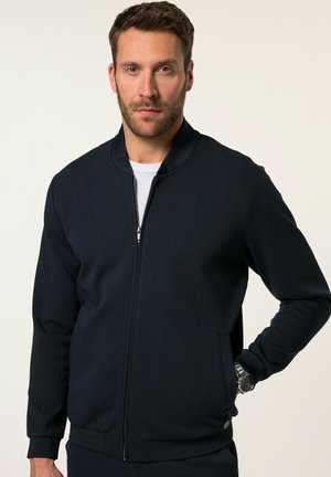 Chaqueta bomber de color azul marino oscuro con cierre de cremallera en el frente, puños de canalé y bolsillos laterales. Fabricada en un tejido suave y texturizado con un acabado de cuello liso.