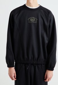 Czarna bluza z prążkowanym dekoltem, elastycznym dołem i mankietami. Na piersi zielone, haftowane logo "Fantasy Fussball Club".