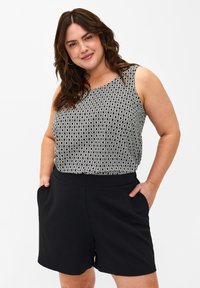 Pantaloni corti neri con cintura elastica, abbinati a una maglietta senza maniche con un motivo geometrico in bianco e nero.