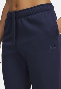 Námornícke modré tepláky s elastickým pásom, nastaviteľnou šnúrkou a vyšitým logom Under Armour na ľavom stehne. Mäkká textúra látky.