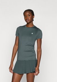 Tamsiai žalia sportinė marškinėliai su trumpomis rankovėmis ir apvaliu iškirpimu, derinami su suderinta sijonu. Audinys atrodo lygus, su minimaliais dizaino akcentais.