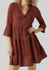 Vestido de color óxido con capas y escote en V, con mangas acampanadas de tres cuartos. Hecho de una tela texturizada, con una silueta fluida.