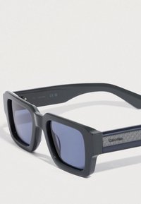 Čtvercové sluneční brýle s tmavě šedým plastovým rámem, modře tónovanými čočkami a texturovanými tmavě šedými bočními rameny zdobenými geometrickým vzorem.