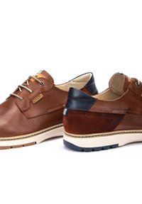Zapatos de cuero marrón con textura perforada, detalles en azul marino en el talón, suela beige y costuras beige. Diseño de cordones.