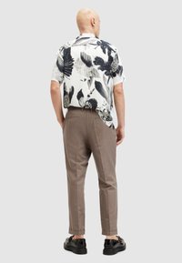 Camisa de manga corta con un estampado floral en blanco y negro, combinada con pantalones marrón claro y zapatos negros. Tejido suave, corte relajado.