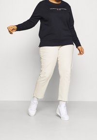 Felpa navy con logo, pantaloni dritti color crema e sneakers bianche. La felpa ha maniche lunghe e polsini a coste; i pantaloni presentano orli sfrangiati.