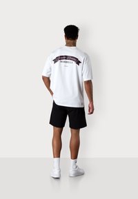 T-shirt blanche avec un graphique noir et rose au dos portant l'inscription "Summer Romance MARBELLA". Associé à un short noir et des baskets blanches.