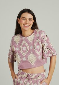Kurzärmeliges, kurzes Oberteil aus helllila Baumwolle mit weißen gestickten Blumen- und Diamantmustern, akzentuiert mit Spitze und gewellten Kanten.