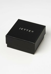 Schwarze Geschenkbox mit strukturierten Oberflächen, die ein silbernes "JETTE"-Logo auf dem Deckel aufweist. Quadratische Form mit leicht erhöhtem, klappbarem Deckel.