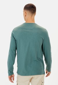 Teal langærmet skjorte lavet af letvægtsstof, med en rund halsudskæring, sideslids og en tekstureret finish. Enkel og glat design.