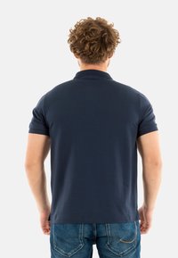 Camisa polo azul marino de manga corta, con un cuello clásico y un dobladillo recto, hecha de suave tejido de algodón. Combinada con unos jeans de mezclilla claros.
