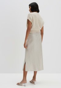 Beiger, kurz geschnittener Strickpullover mit weiten Ärmeln, kombiniert mit einem hellgrauen, leichten Maxirock aus Leinen, der einen Seitenschlitz hat. Silbersandalen runden das Outfit ab.