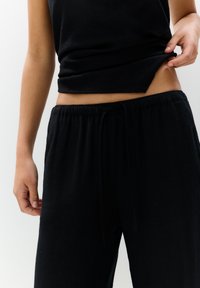 Haut noir sans manches et pantalon noir ample. Le tissu semble doux avec une taille élastique et un cordon de serrage.