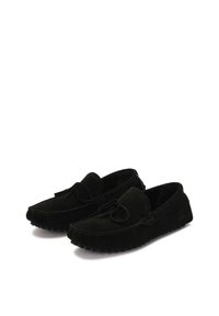 Mocasines de ante negro con punta redondeada, adornos de lazo decorativos y suela de goma con pequeños protuberancias para un mejor agarre y flexibilidad.