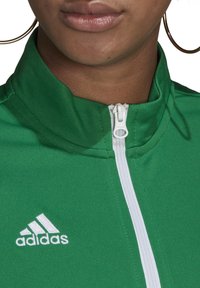 Grön zip-up jacka gjord av textil som har en vit dragkedja och en vit Adidas-logotyp på vänster sida av kragen.