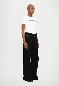 White fitted shirt with black embroidered text, paired with loose black jeans featuring a high waist, simple button closure, and minimalistic design.
