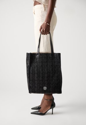 Zwarte tote bag met een gestructureerd, patroon oppervlak en gladde leren handvatten. Zilveren logo detail aan de onderkant. Gekocht met lichte broek.