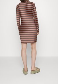 Těsně přiléhavé šaty s dlouhými rukávy, zdobené střídajícími se hnědými a krémovými vodorovnými pruhy. Kombinované s olivovými platformovými sandály.