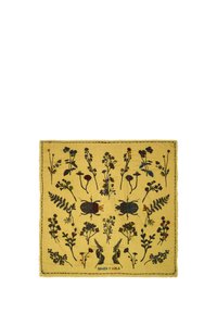 Żółta tkanina z kwiatowym i owadzim wzorem w ciemnych kolorach. Krawędzie są wykończone frędzlami, na dole znajduje się metka "Bimba y Lola".