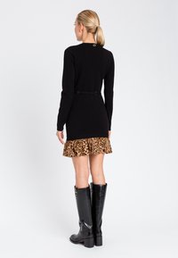 Abito in maglia nero con maniche lunghe, caratterizzato da un orlo a volants con stampa leopardata e una cintura sottile. Indossato con stivali al ginocchio neri lucidi.