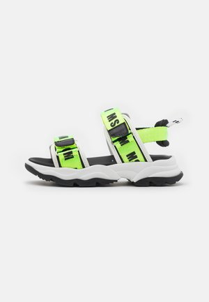 Sandalhas de desporto com sola negra, base branca e alças ajustáveis verdes brilhantes com texto em negrito preto. Alças texturizadas para maior aderência.