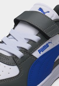 Λευκό και γκρι αθλητικό παπούτσι Puma με μπλε λεπτομέρεια, λευκά κορδόνια και γκρι λουράκι βέλκρο στο πάνω μέρος.