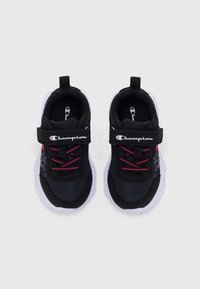 Une paire de baskets Champion pour tout-petits en noir et blanc avec des lacets roses, des motifs d'étoiles sur les côtés et des bandes Velcro sur fond blanc.