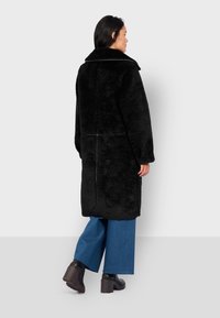 Cappotto in pelliccia sintetica nera con un ampio colletto, maniche lunghe e taglio dritto. Abbinato a pantaloni in denim blu a gamba larga e stivali neri chunky.