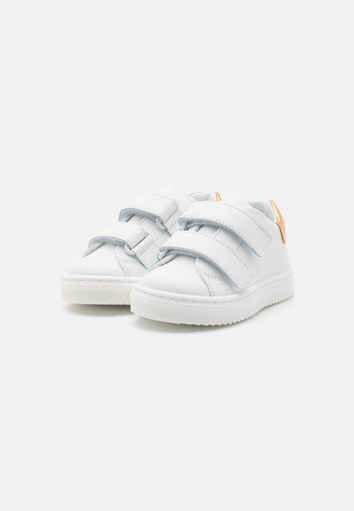 Baskets en cuir blanc avec deux bandes Velcro ajustables et une semelle en caoutchouc texturée ; présente une subtile accent doré au talon.