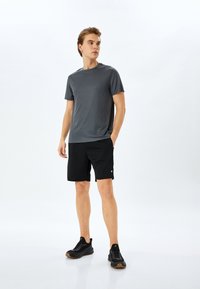 Heren sportoutfit met een donkergrijze shirt met korte mouwen en zwarte shorts, beide gemaakt van lichtgewicht materiaal, gecombineerd met zwarte sportschoenen.
