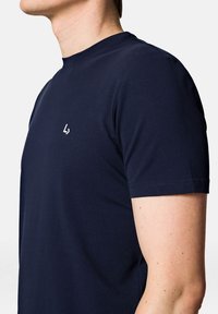 Granatowa koszulka z krótkim rękawem, wykonana z miękkiej bawełny, z okrągłym dekoltem i małym białym logo na piersi. Regularny krój.